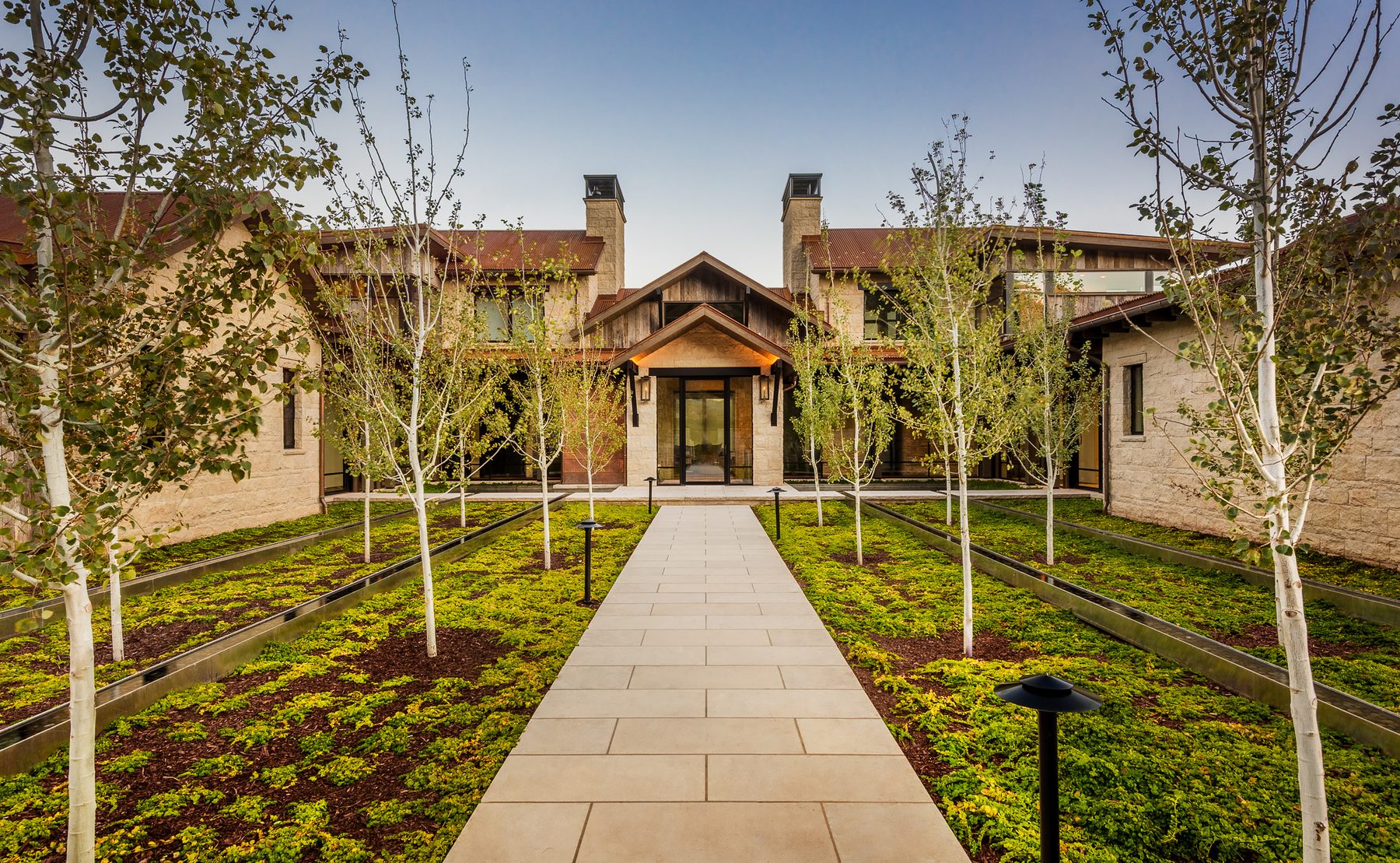 Stone residence entry courtyard lined with aspens